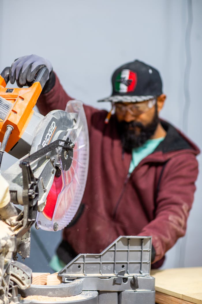 A focused carpenter operates a miter saw during woodworking project, emphasizing safety and precision.