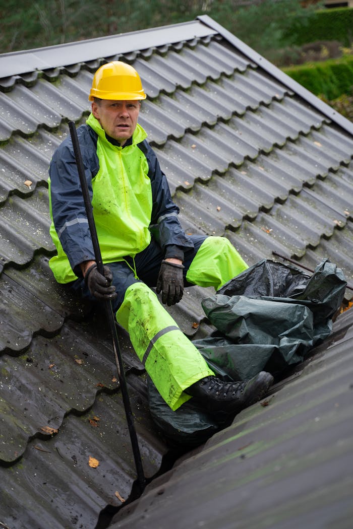 A construction worker in safety gear performing roof maintenance outdoors.